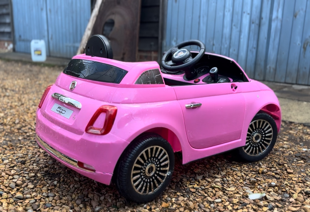Pink Fiat 500 ride-on toy car parked outdoors